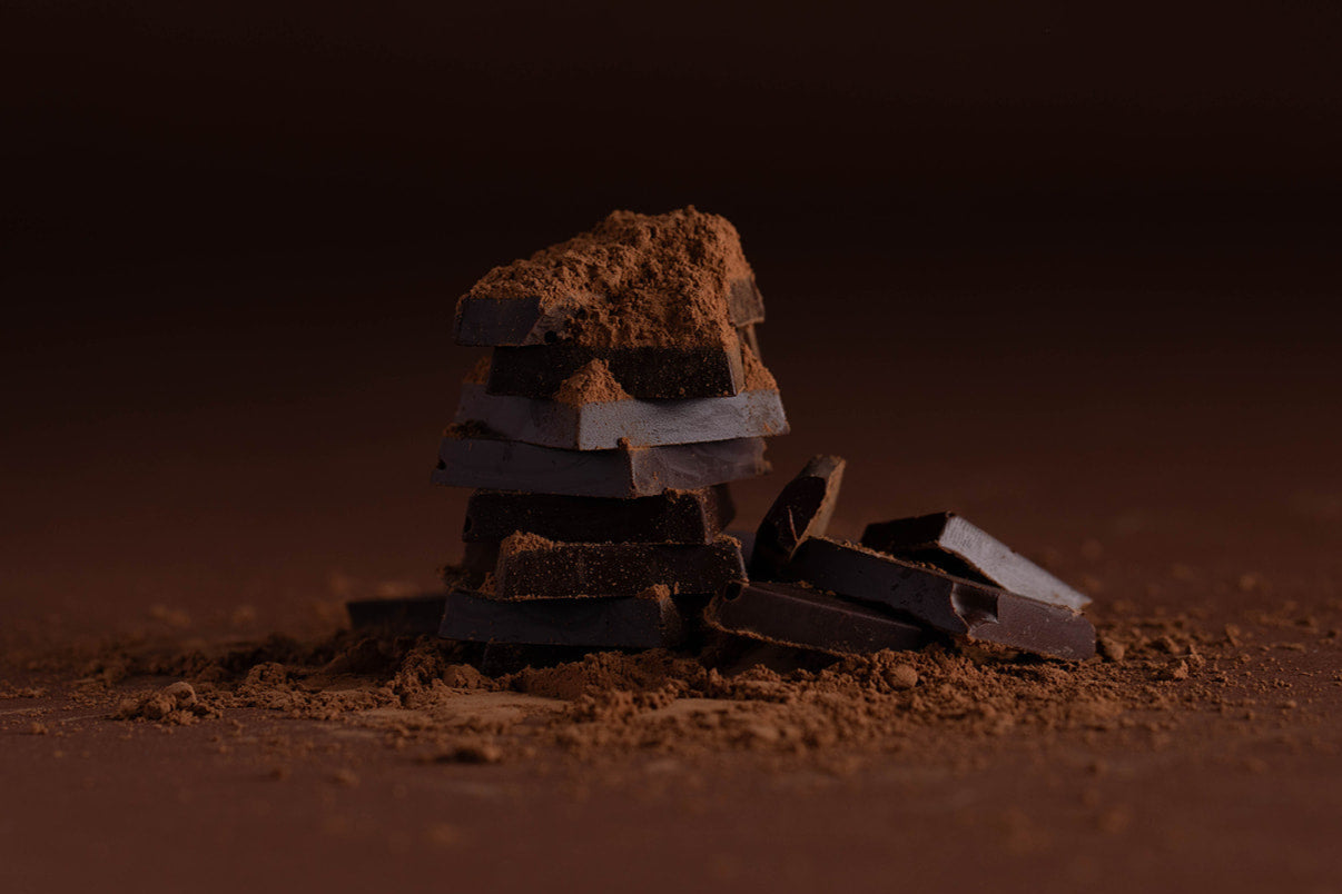 Stack of dark chocolate bars on a dark background dusted in a layer of cocoa powder